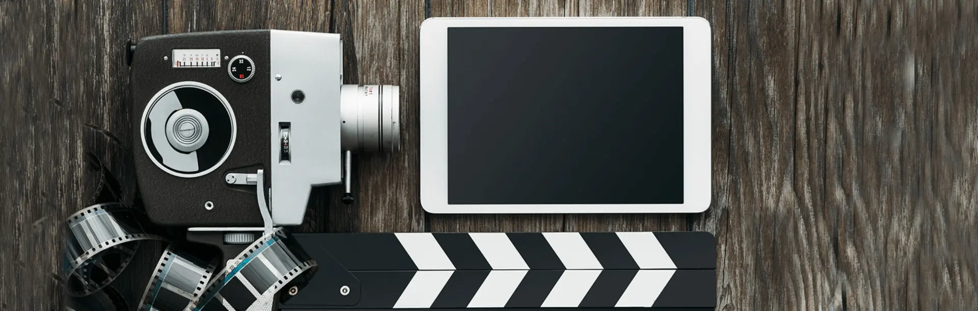 Vintage film camera with film reel, clapperboard, and tablet on wooden surface
